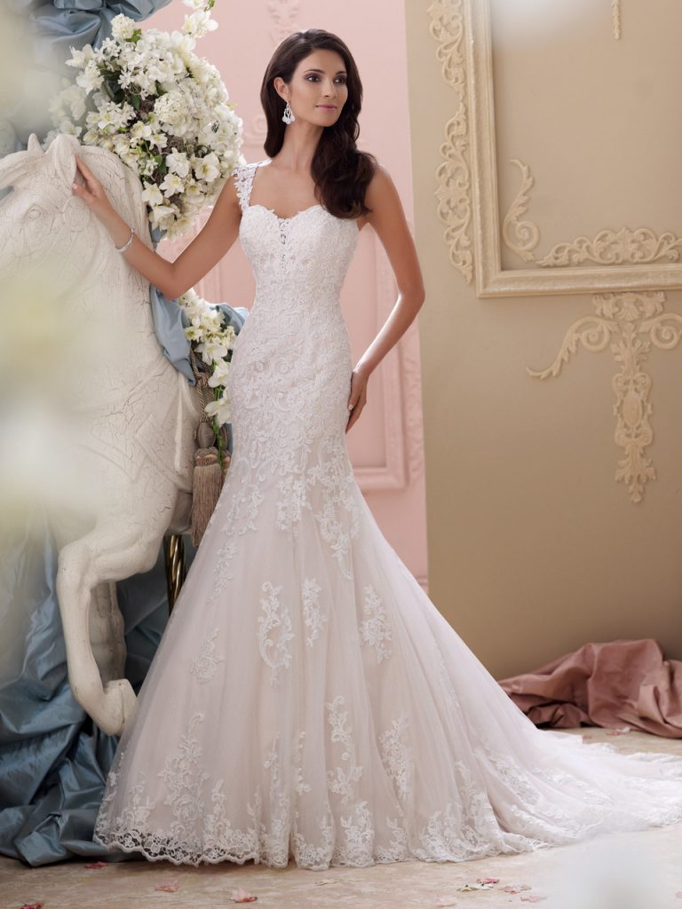 Vestido de Noiva com manga curta, leve transparência no decote frente e decote profundo nas costas, todo em renda rebordada com pedrarias, corpo alongado e saia semi sereia, leve cauda.